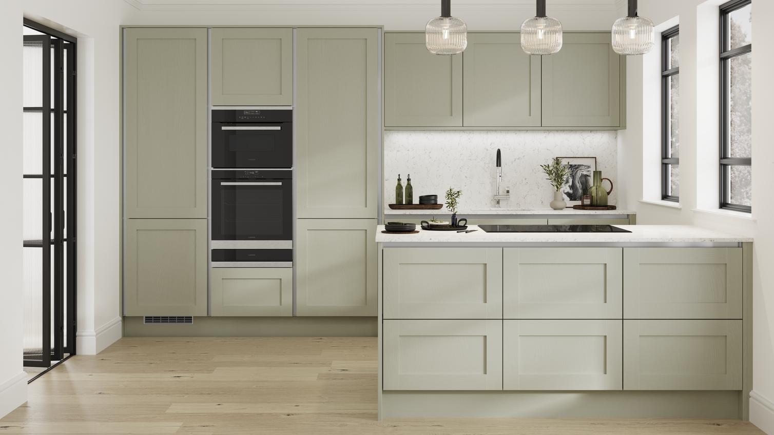 A shaker kitchen with sage-green doors, white worktops, black double oven, and silver profiles for a modern handleless look.